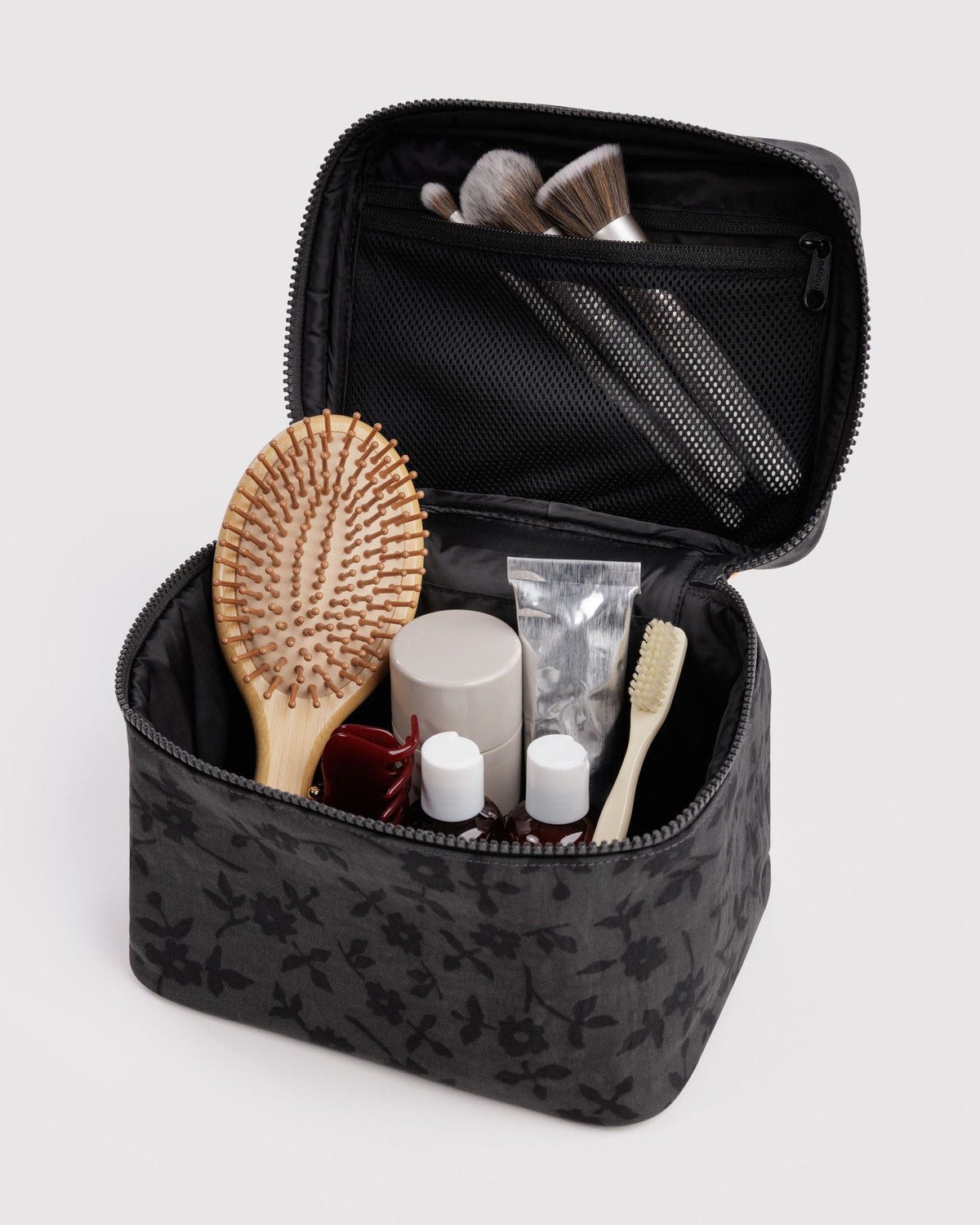 Large charcoal floral cosmetic case open with brushes and small bottles inside.