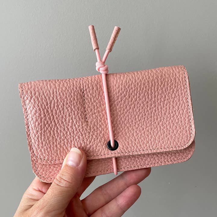 Pink leather knot wallet with front flap and pink cord tie, hand holding wallet