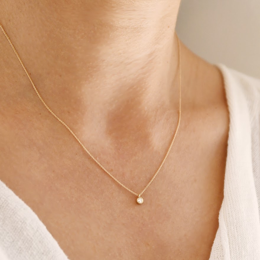 14k gold diamond pendant necklace on neck, small round stone at center
