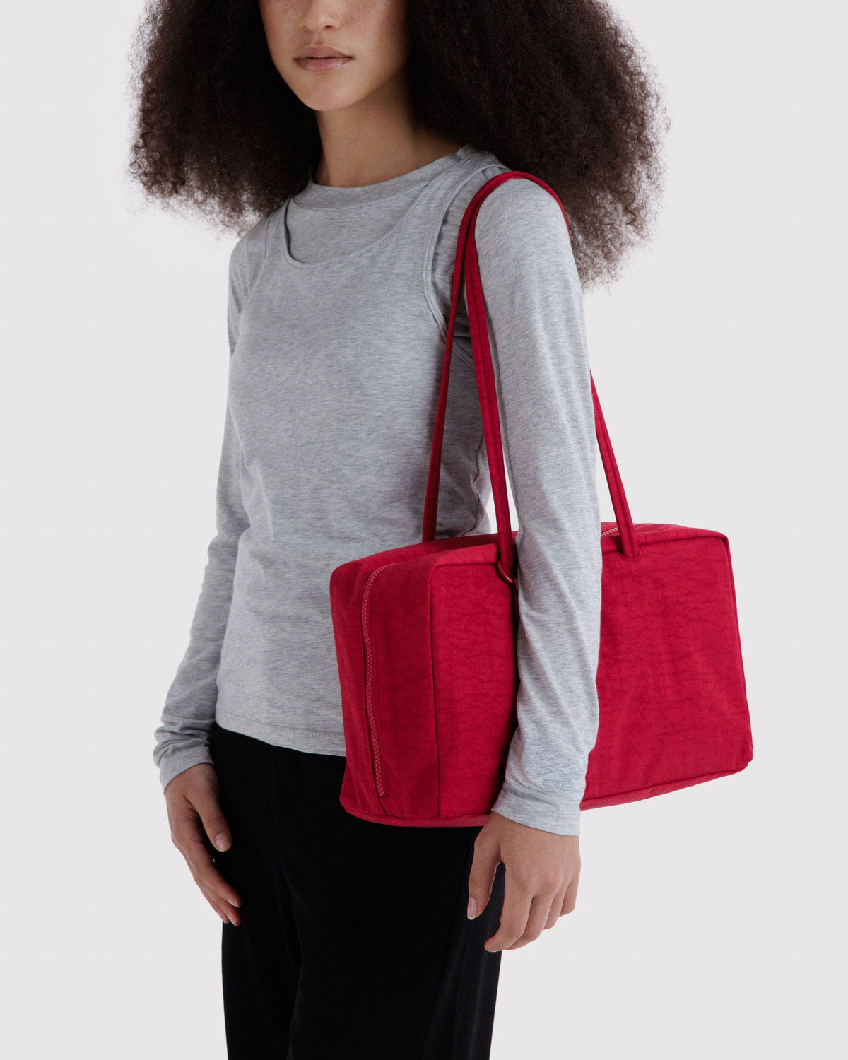 Medium nylon bowler bag held at side; red with top zipper and carry handles.