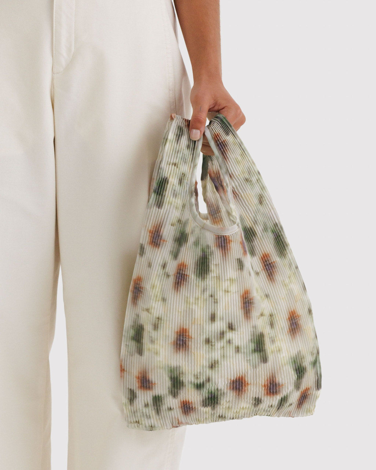 Pleated Baggu tote with cream floral print, held in hand with wide U-shaped opening