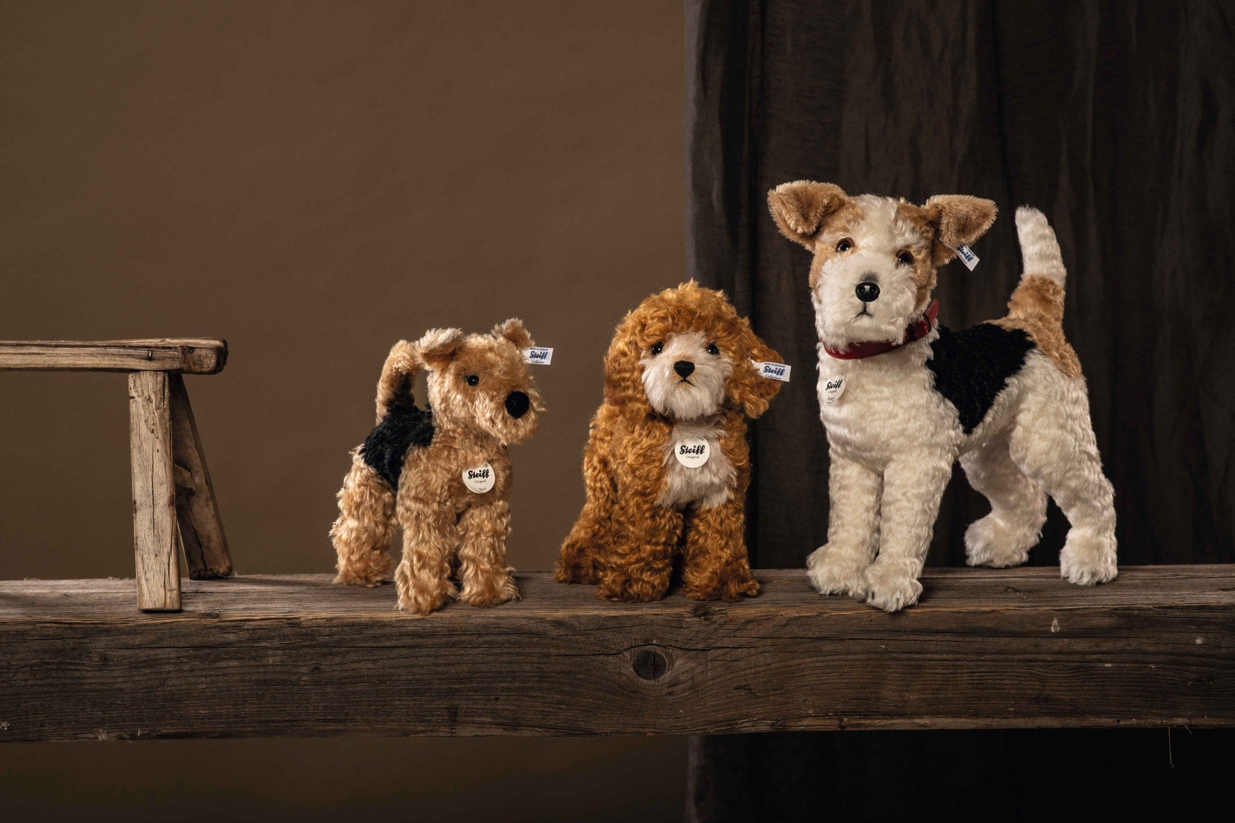 Three plush terrier dogs on a wooden ledge, with Steiff tags, tan and black coats