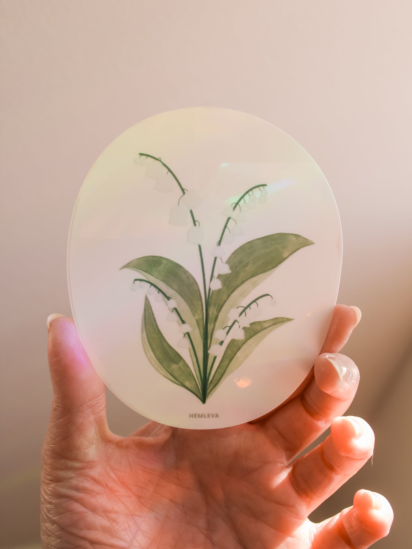 Medium circular suncatcher held in hand, lily of the valley white blooms with green leaves