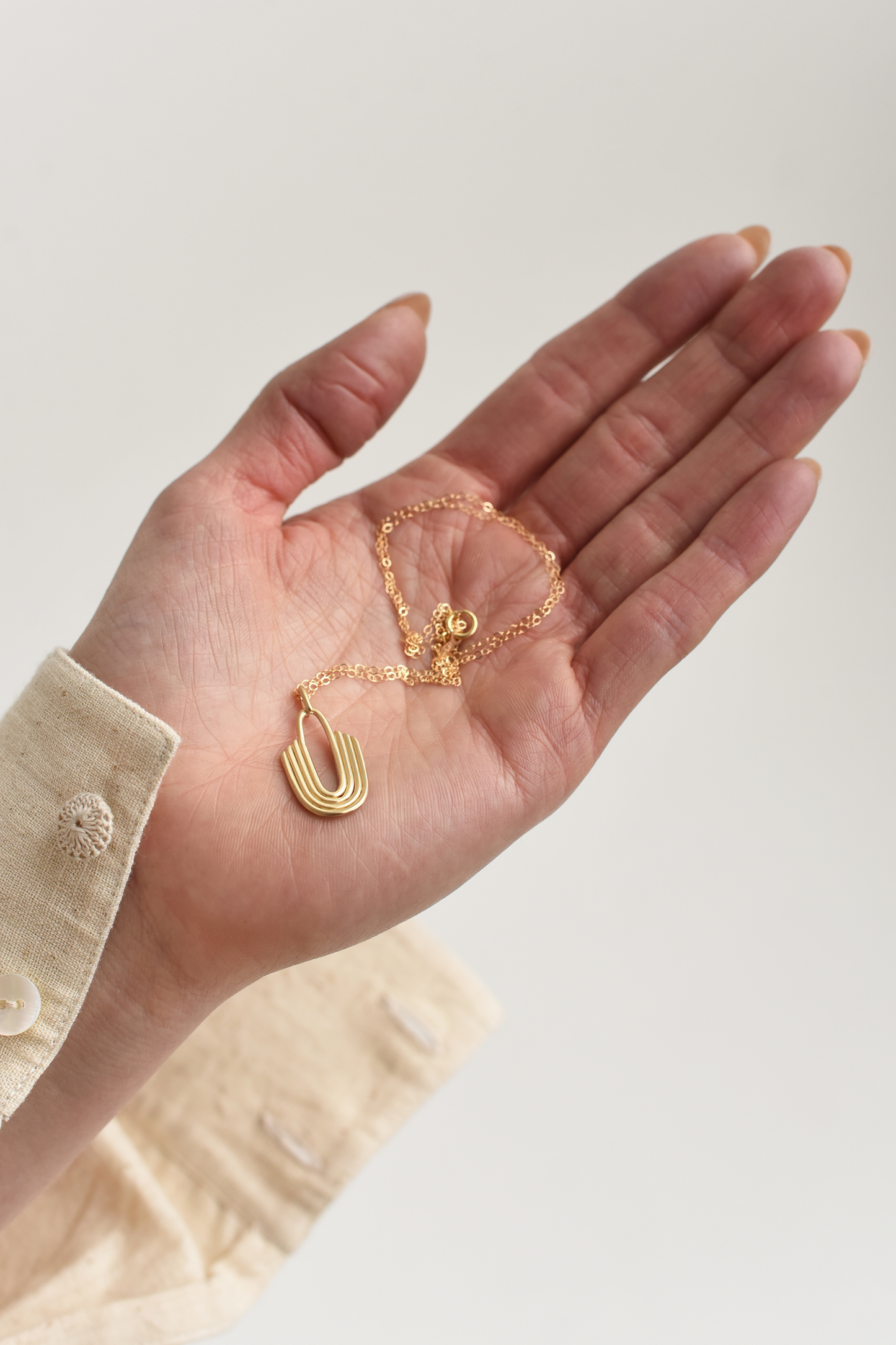 Gold U-shaped layered brass pendant necklace on a fine chain, shown in hand