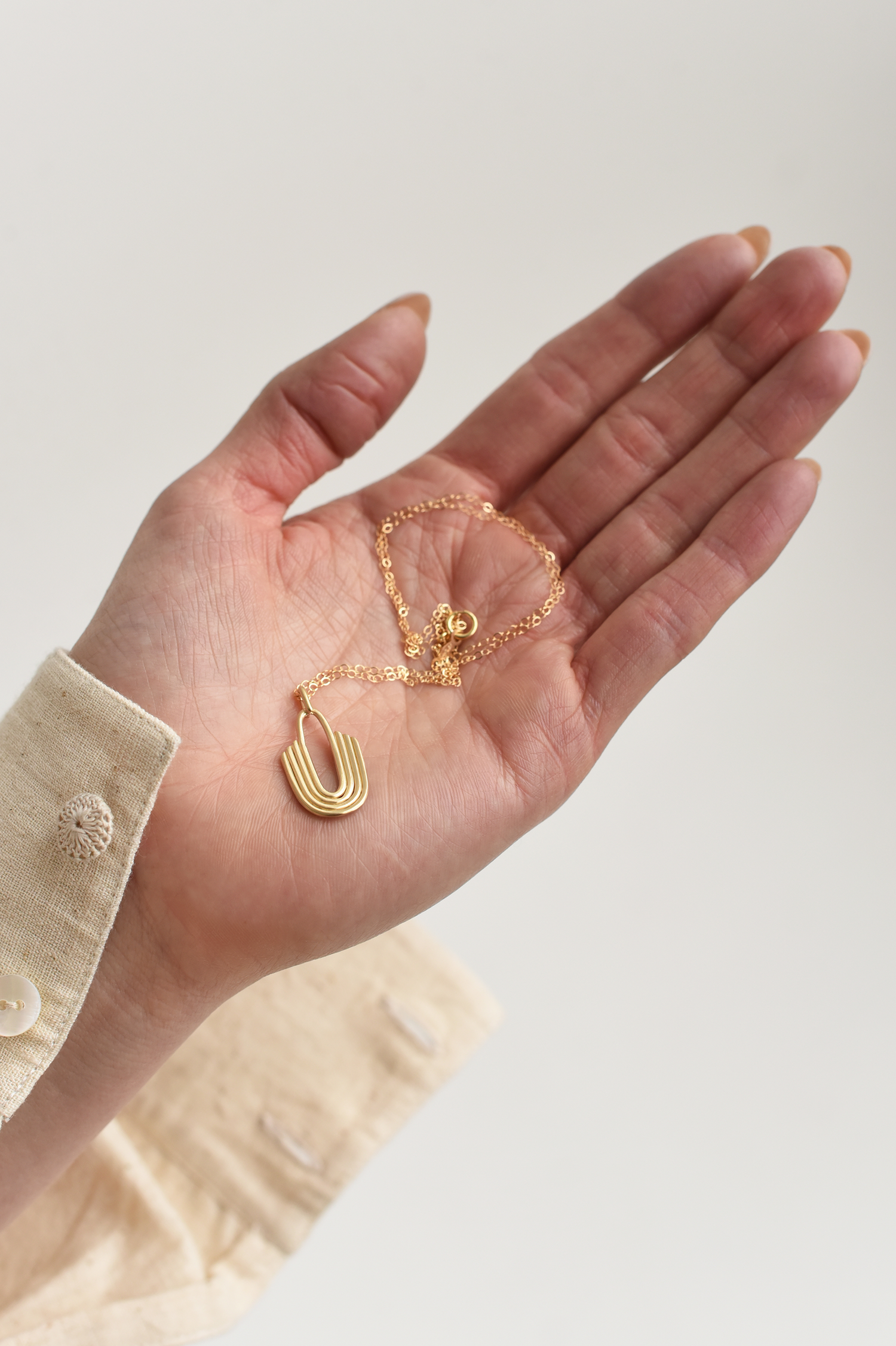 Gold U-shaped layered brass pendant necklace on a fine chain, shown in hand