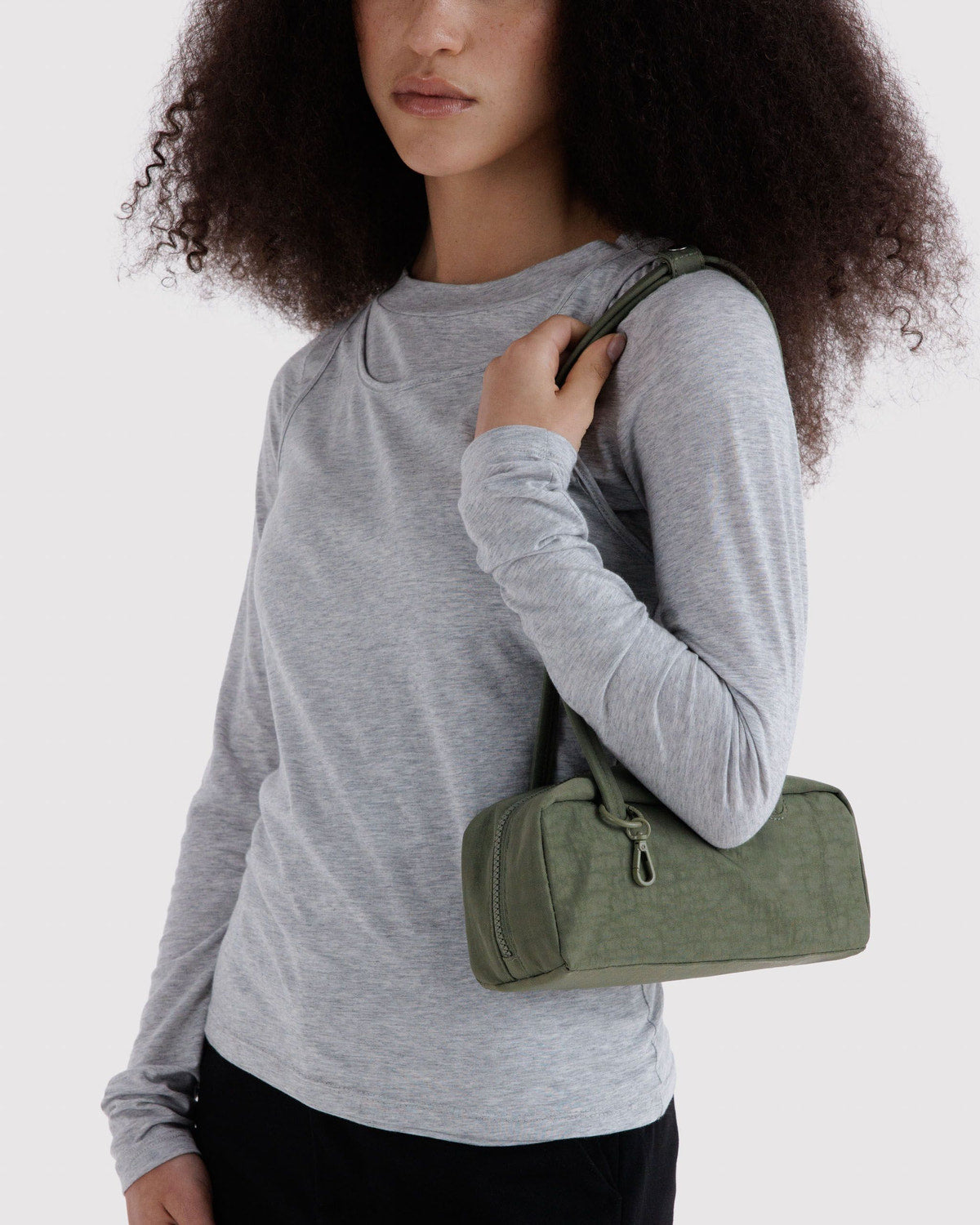Small nylon bowler bag in caper green worn on shoulder, front zip pocket visible.