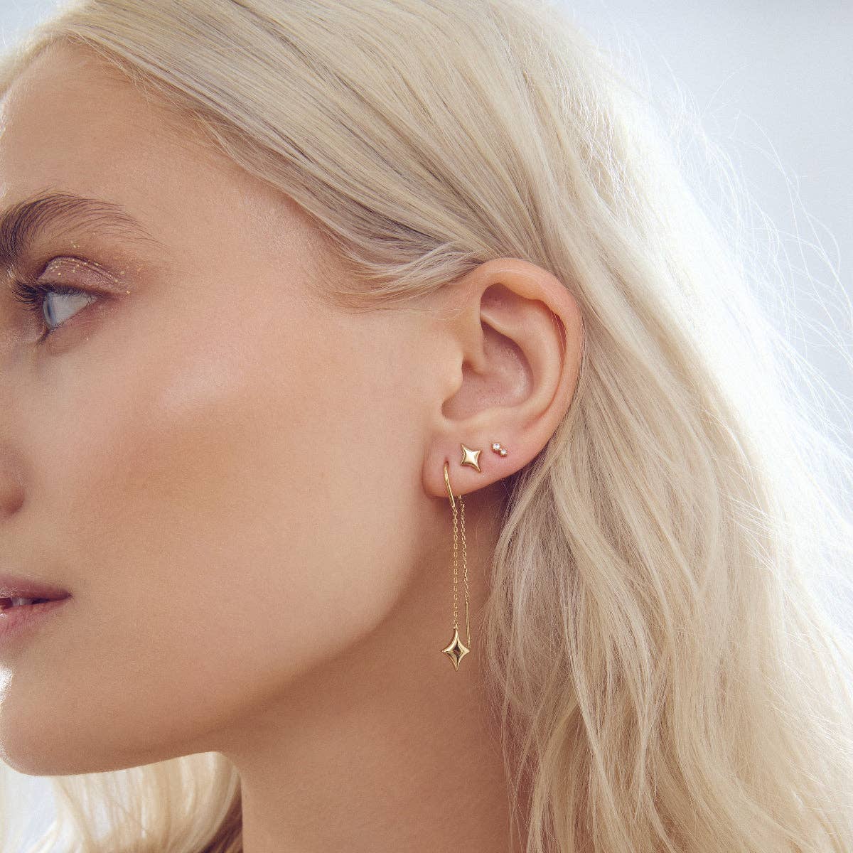 Gold-tone star stud earrings on ear with dangling star drops