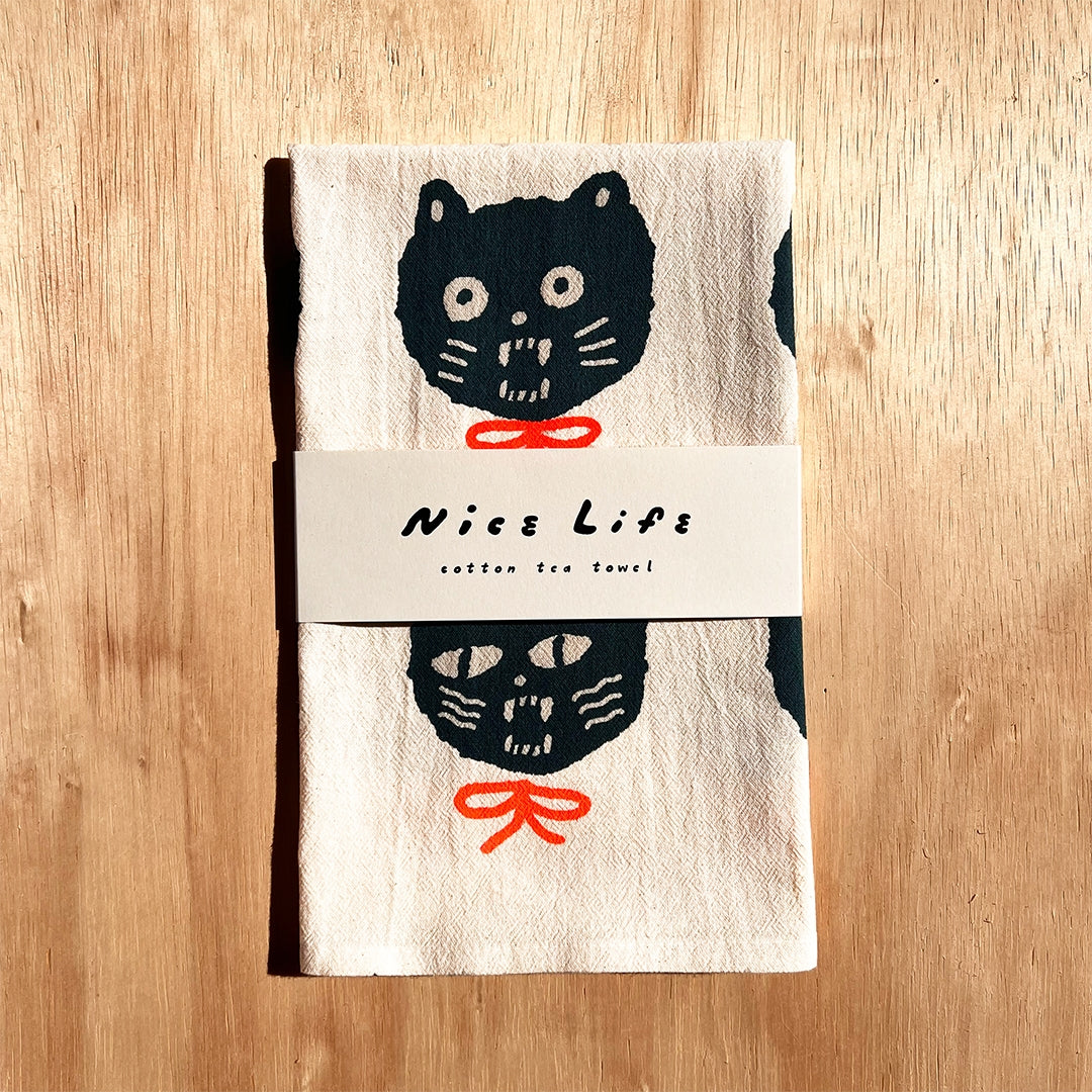 Folded tea towel with single dark cat face and label band, red bow detail