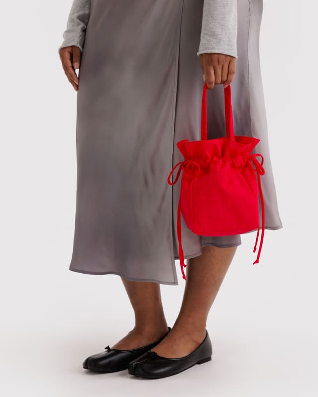 Red nylon drawstring bag with gathered top, held in hand