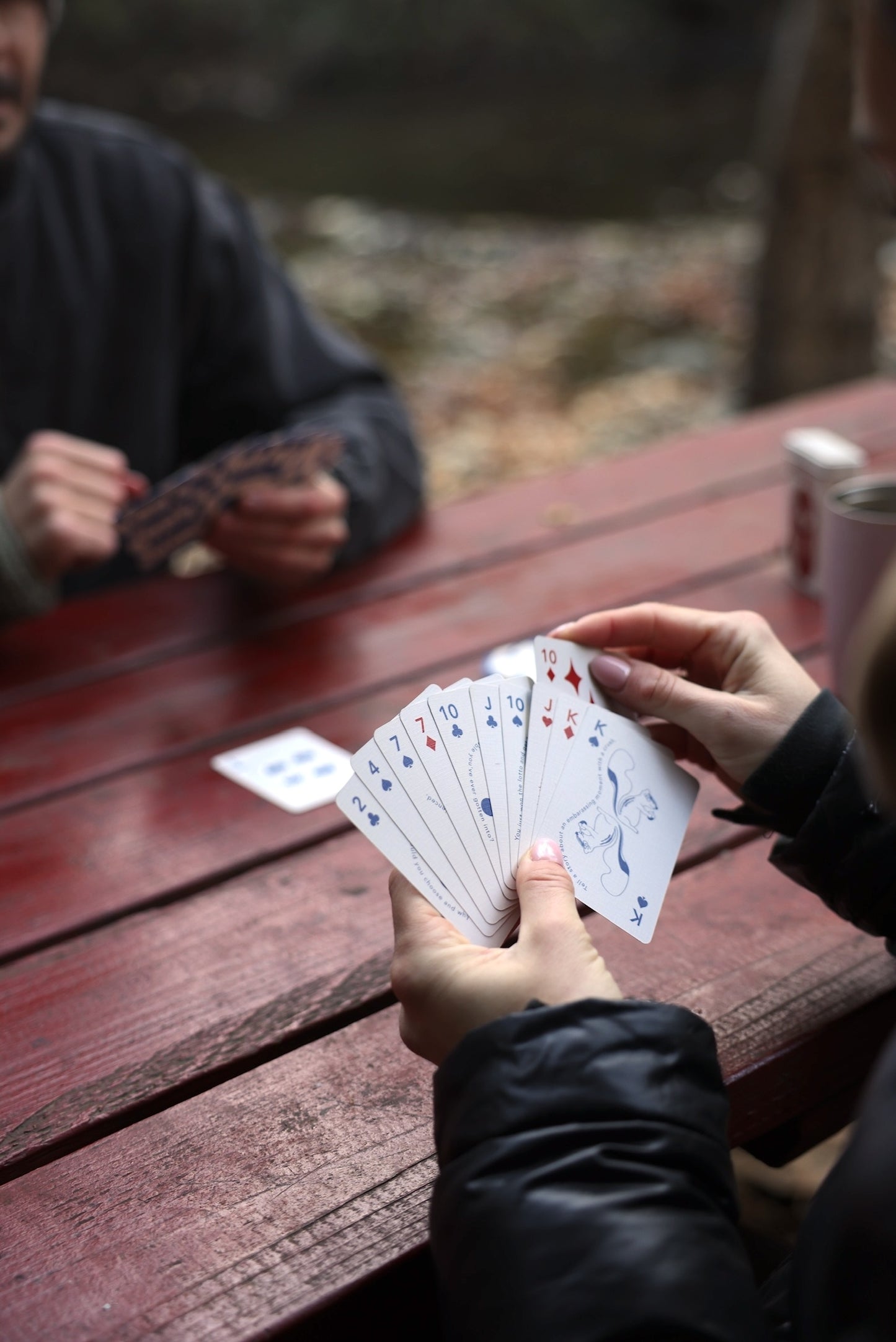 Playing card deck dealt on a wooden table, hands holding multiple cards