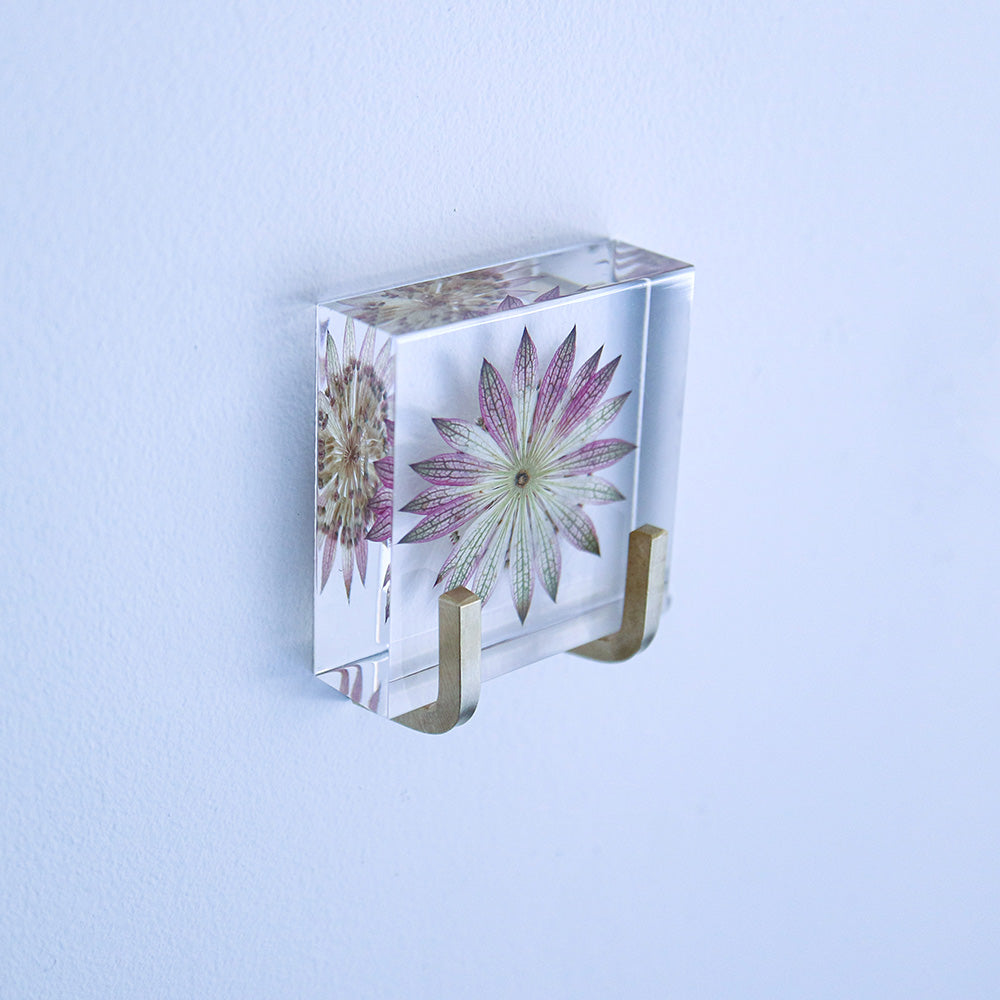 Decorative glass tile with flower print and gold mounting clips, angled view.