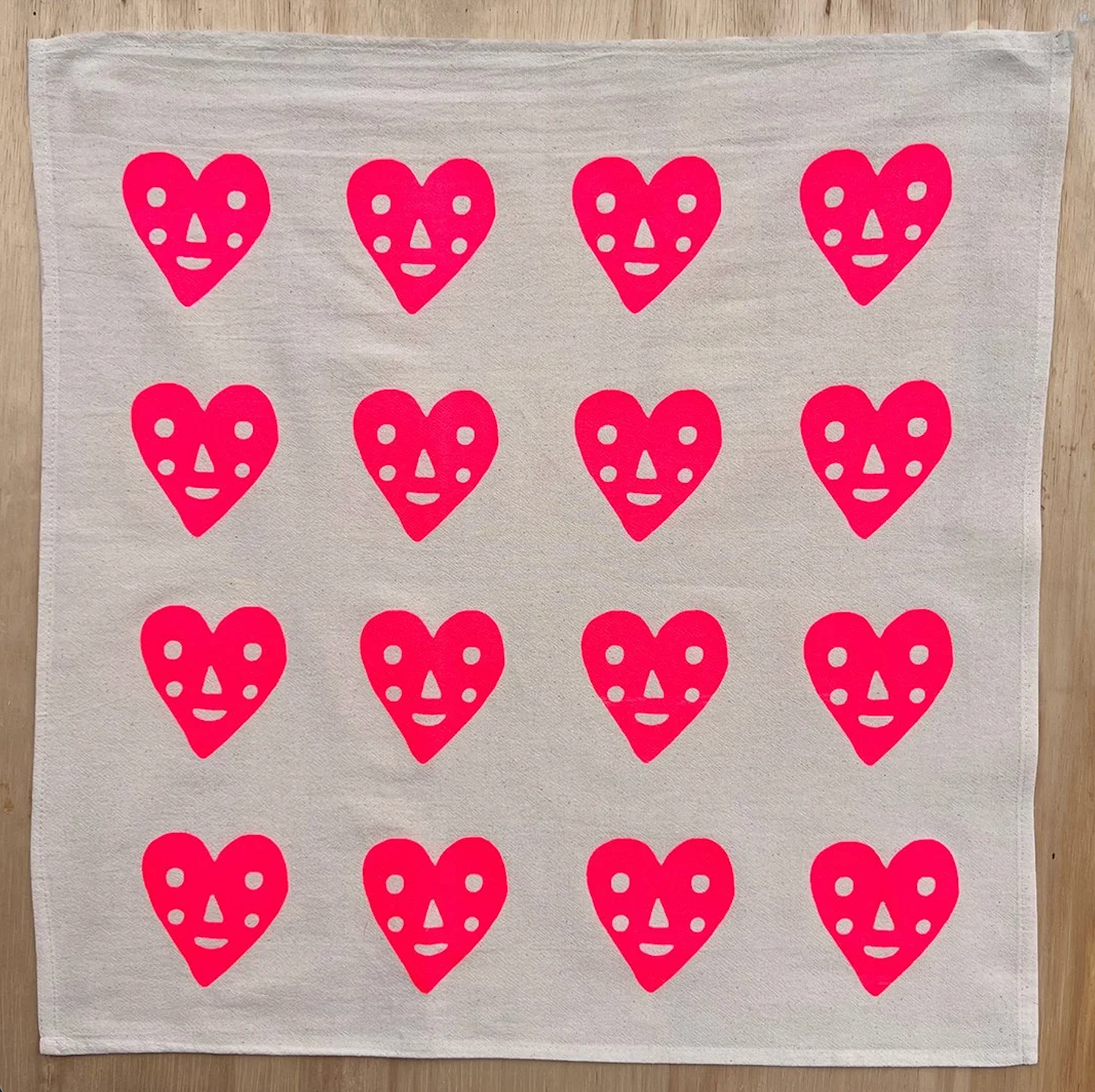Light gray tea towel with repeating pink heart faces pattern