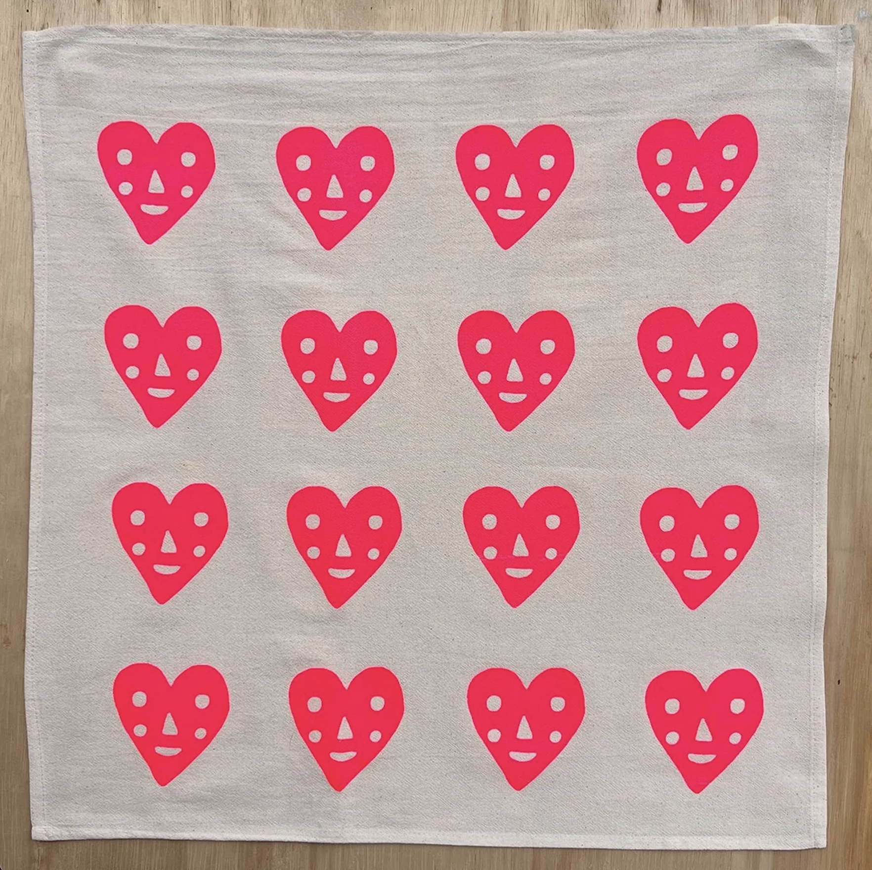 Light gray tea towel with repeating pink heart faces pattern