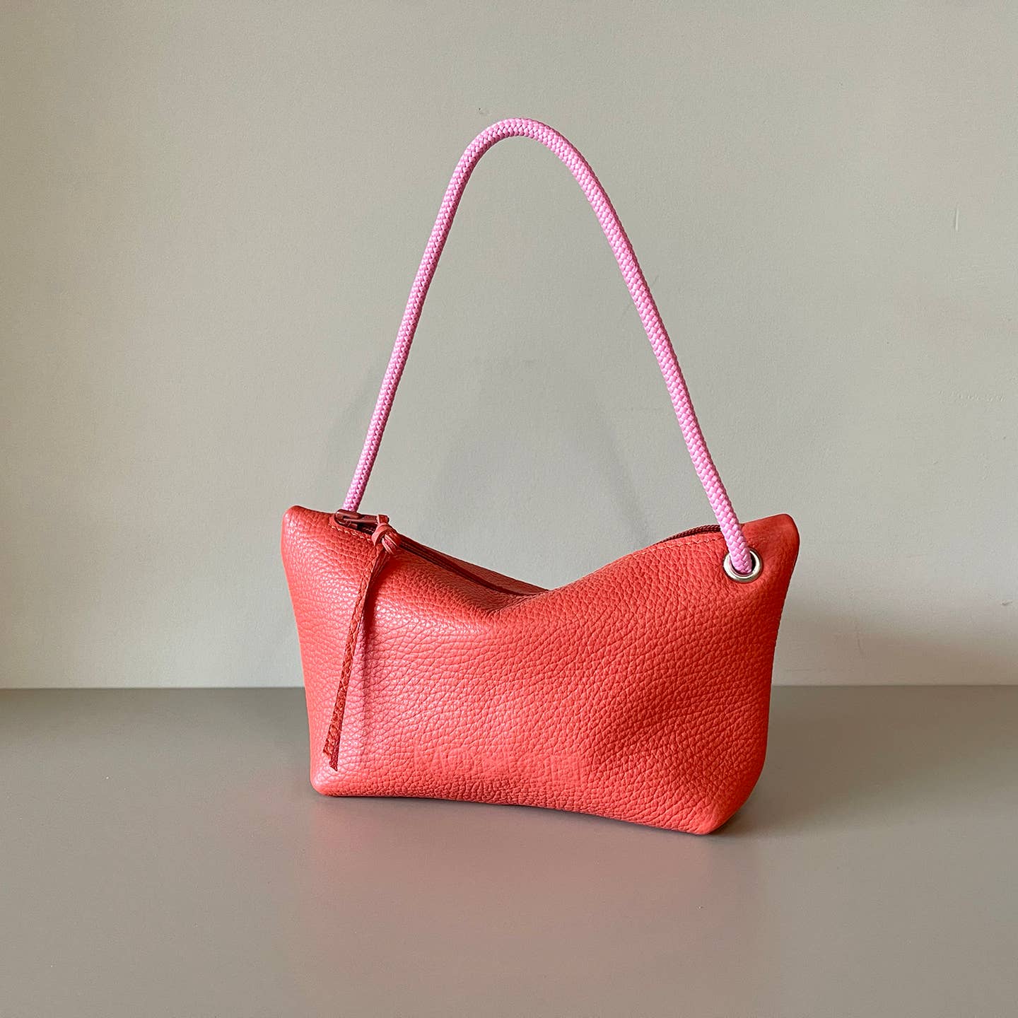 Coral-red cord pouch with pink braided handle and textured leather finish.