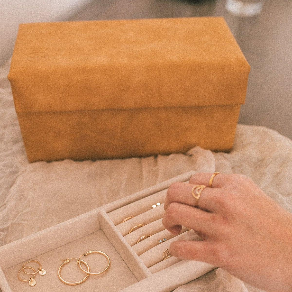 Honey vegan leather jewelry box open with compartments as rings are placed inside.