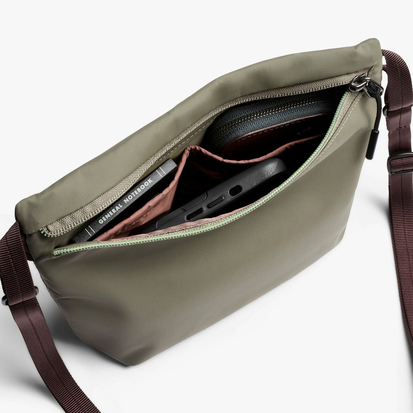 Crossbody bag with olive green interior showing zip pocket and adjustable burgundy strap