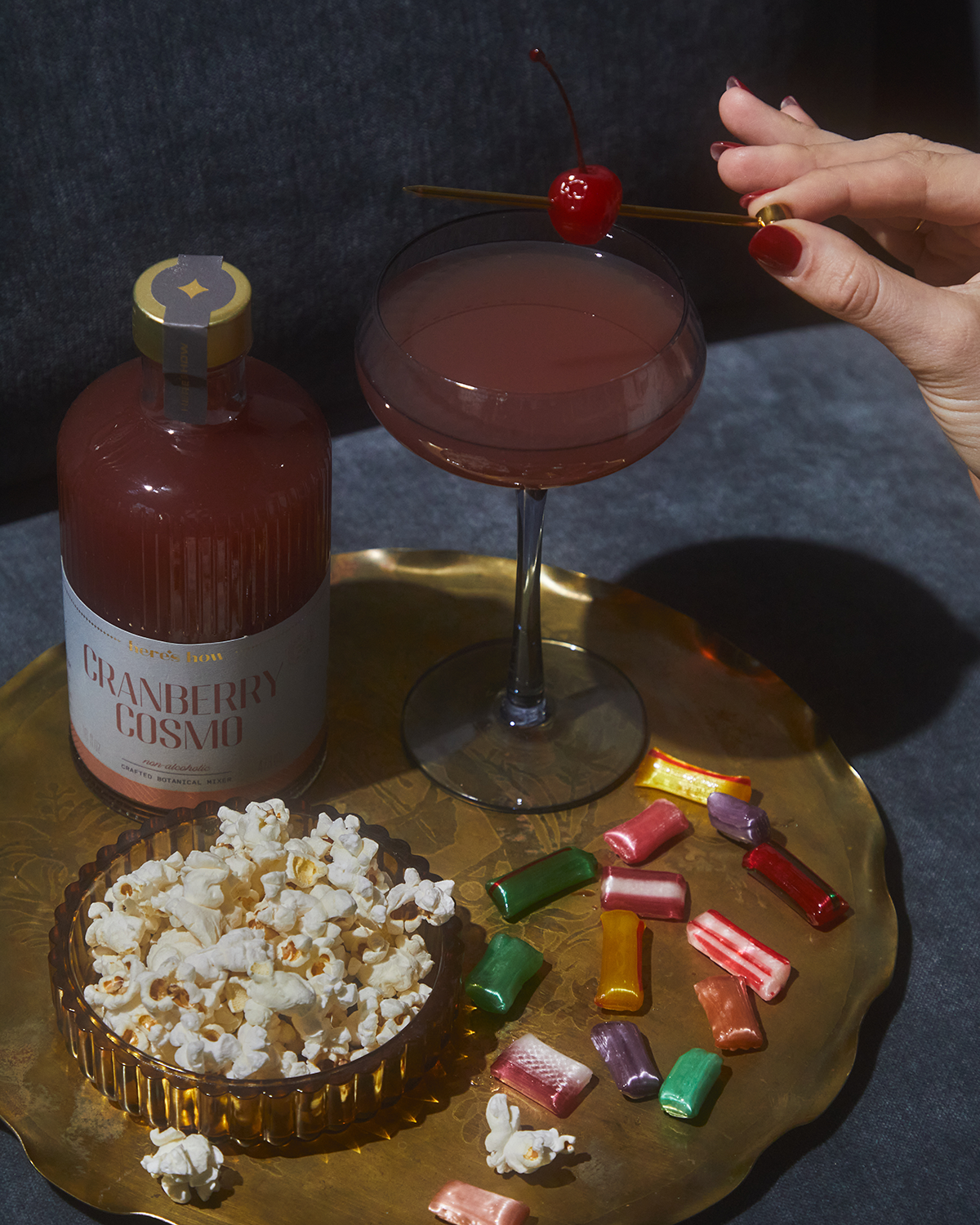 Gold cocktail pick held above a cocktail glass with a red cherry