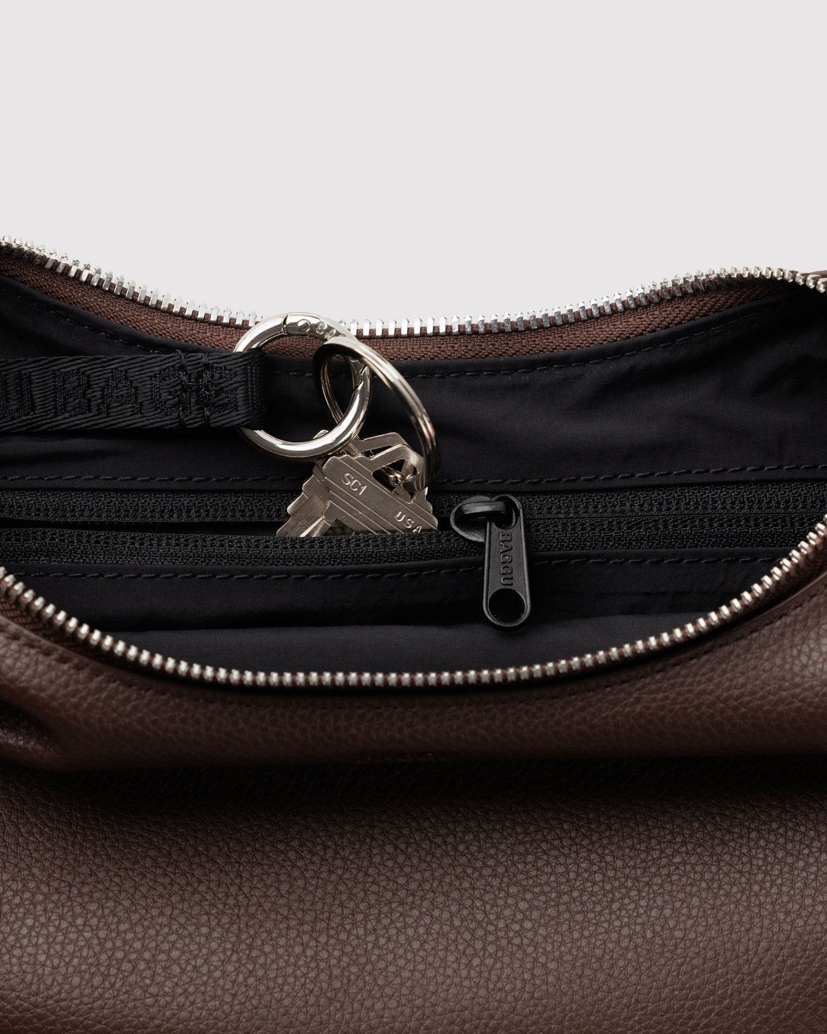 Close-up of zip-top hardware, metal ring and lock on brown recycled leather crescent bag