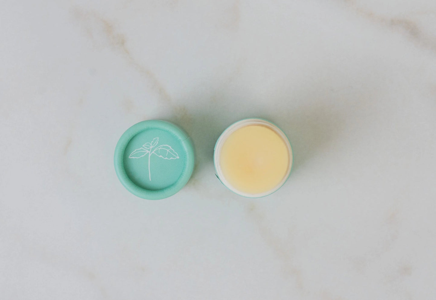 Two open lip butter tins, teal balm and pale yellow balm in round tops
