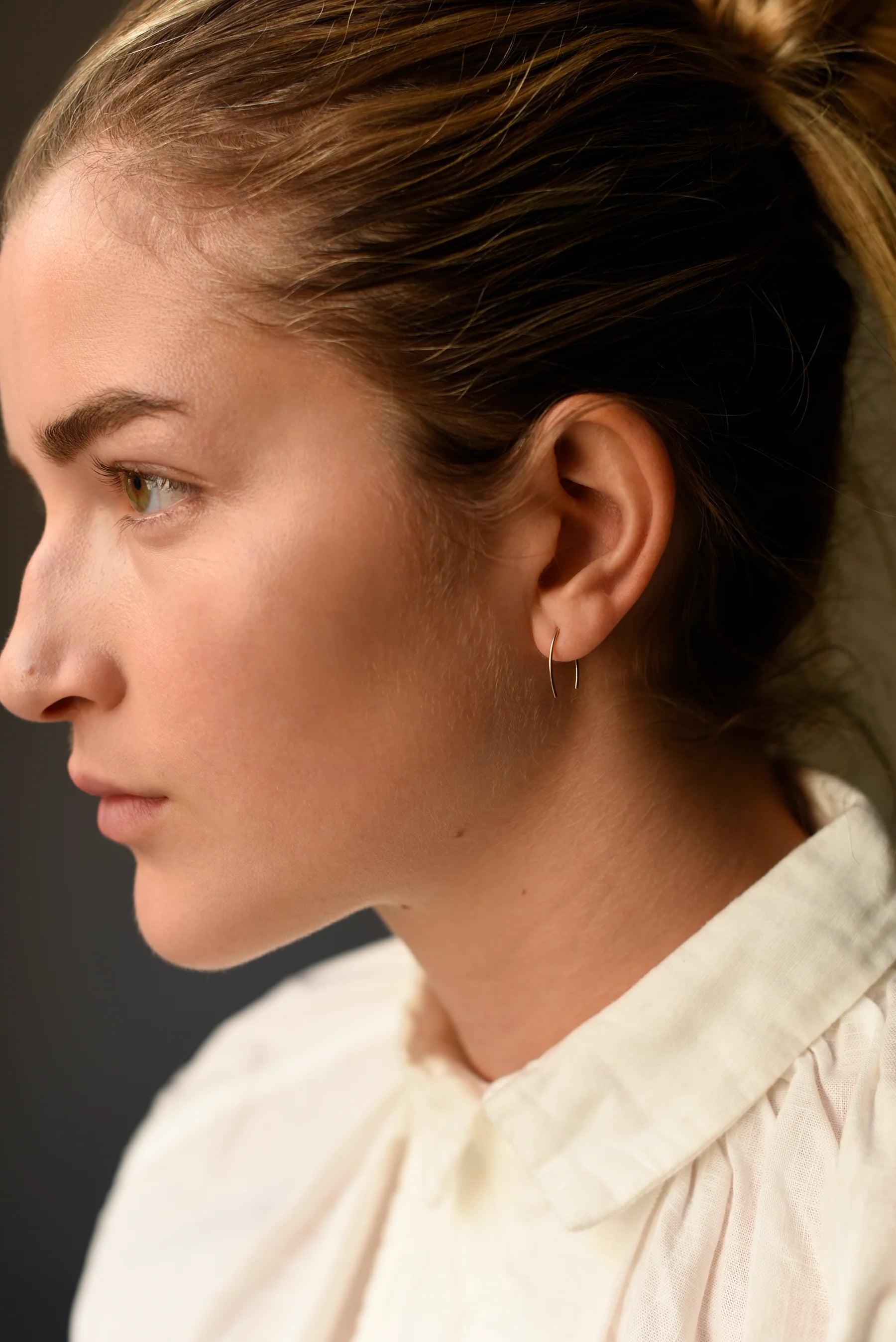 Gold-tone wishbone threader earrings on ear, thin wire with dangling bar