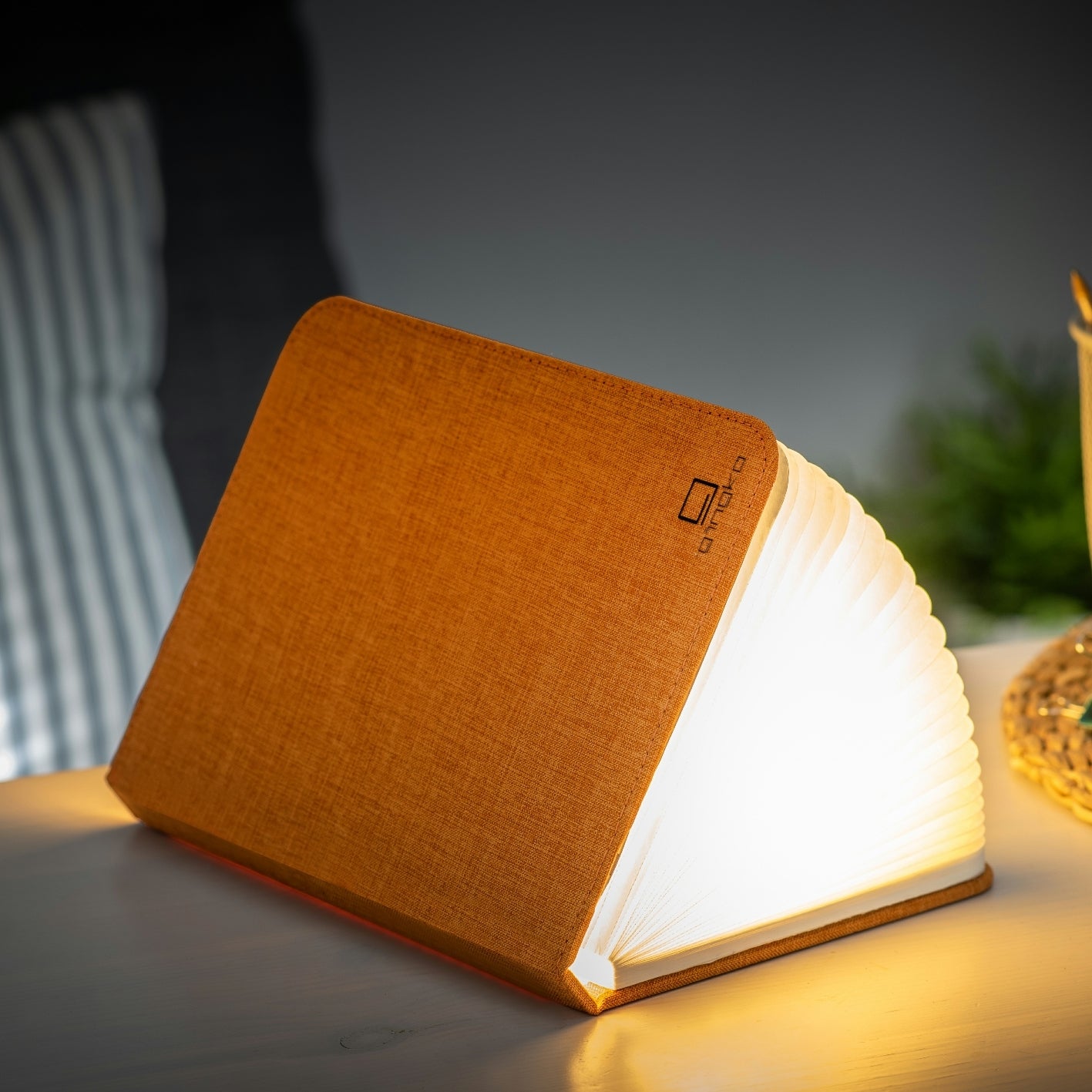 Orange linen smart booklight with glowing LED pages in a tilted stand