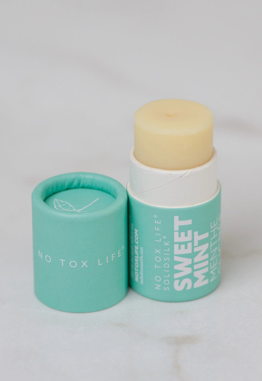 Two lip butter containers, teal base and white tube with beige balm top