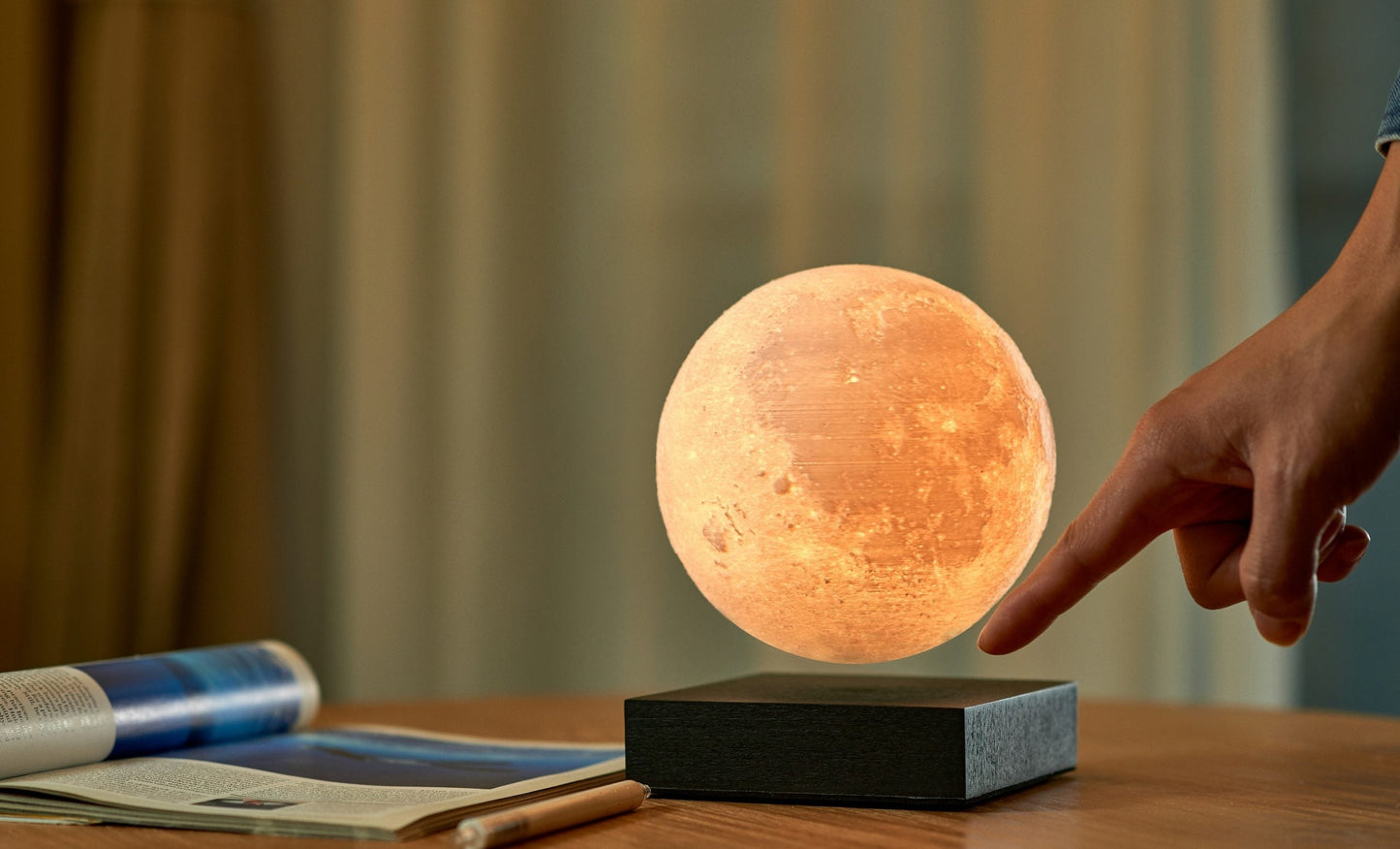 Moon lamp with warm glowing sphere on black base, hand adjusting