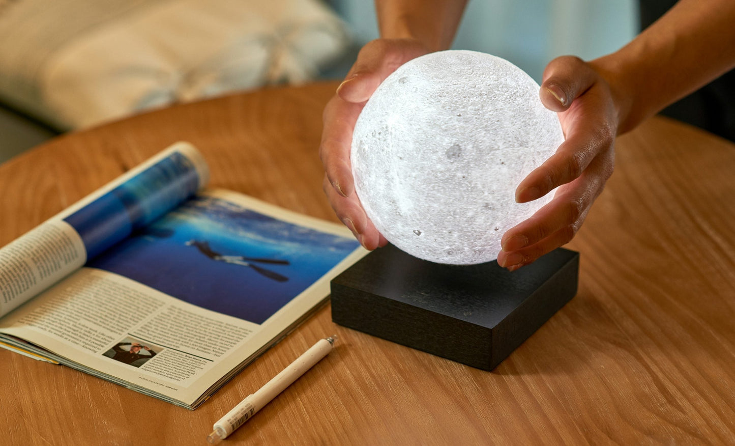 Moon lamp with white glowing sphere on black base, hands holding top
