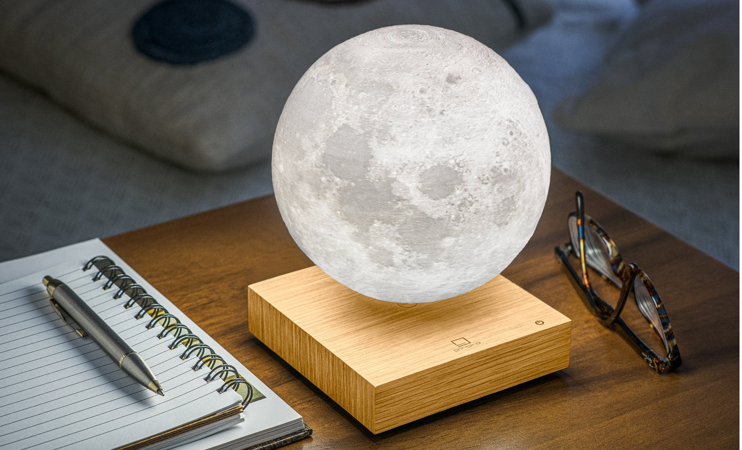 Moon lamp with glowing frosted sphere on light wood base, tilted view