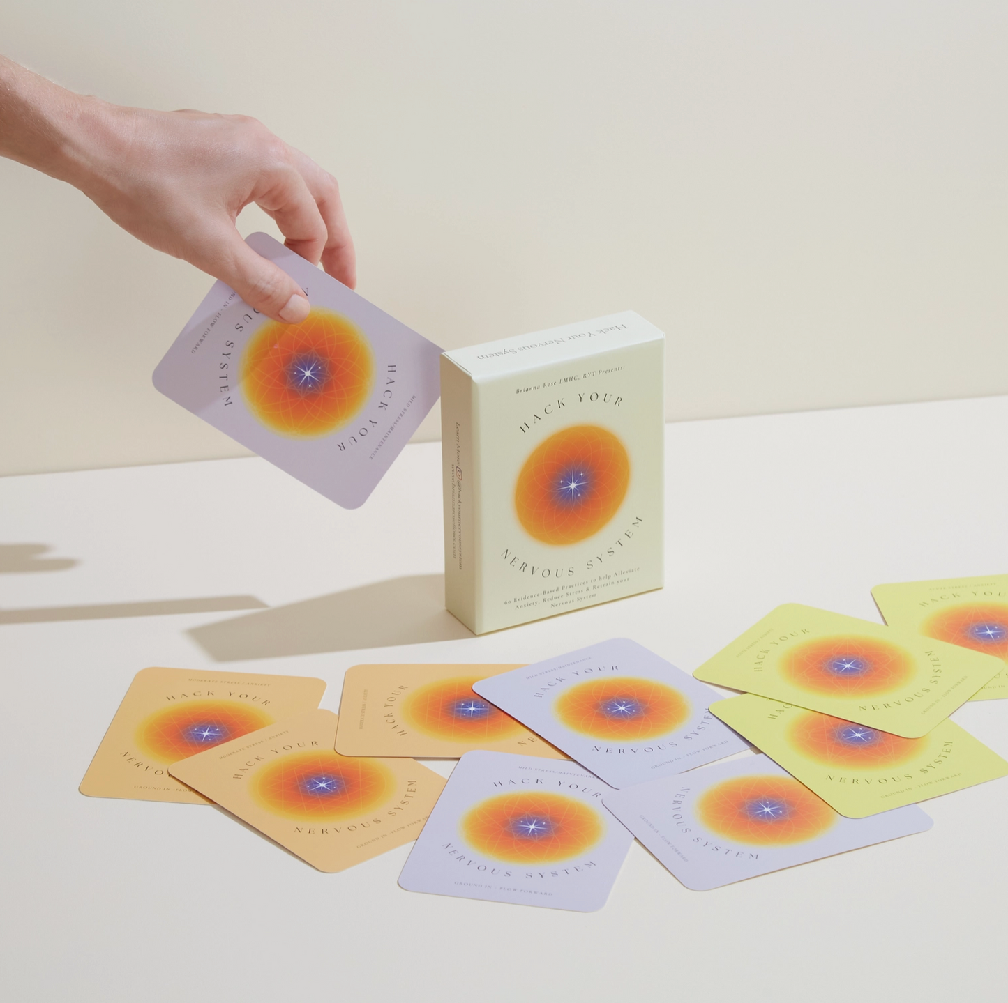 Hand holding one card above spread deck; sunburst with blue center on each card.