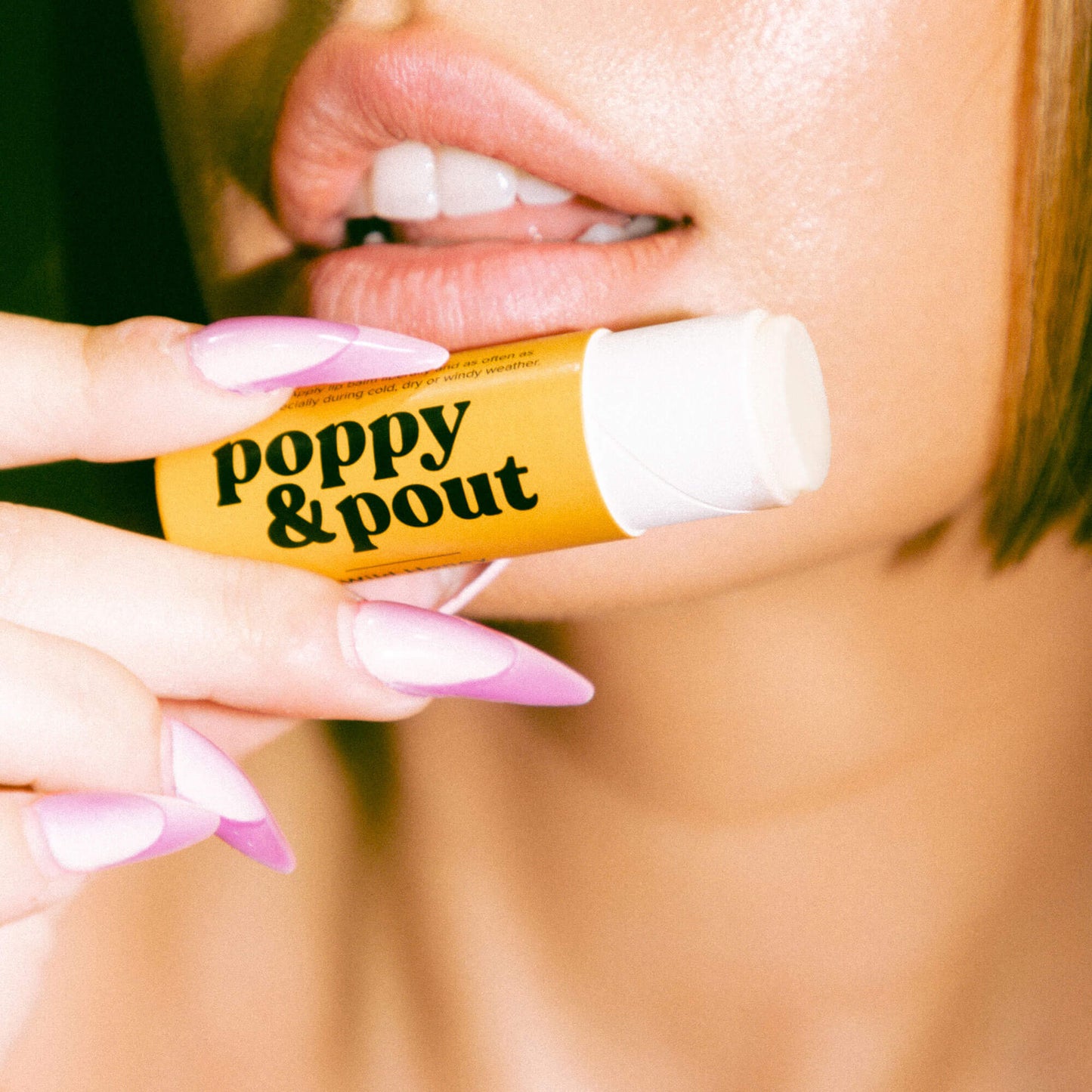 Lip balm being applied from a yellow tube; white balm on lips