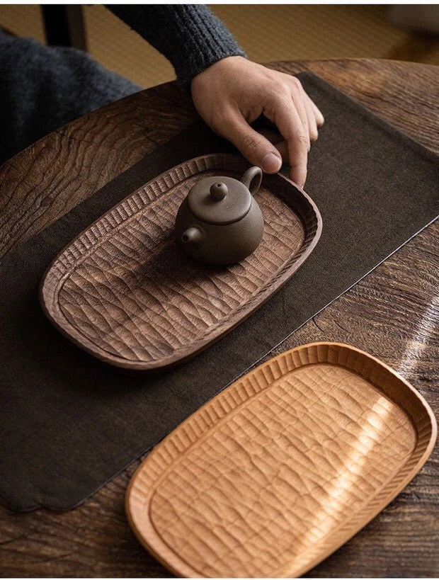 Wooden tea tray with carved border and textured insert, holding a dark teapot and cup