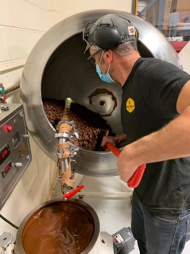 Chocolate-coated almonds in large processing vat with almonds being poured