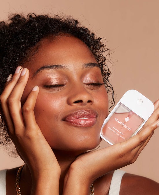 Woman holding a white touchland Power Mist hand sanitizer spray bottle near face