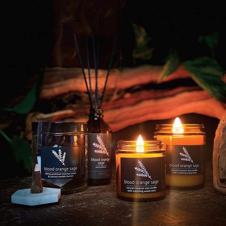 Lit blood orange sage coconut wax candles with wood wicks, amber jars