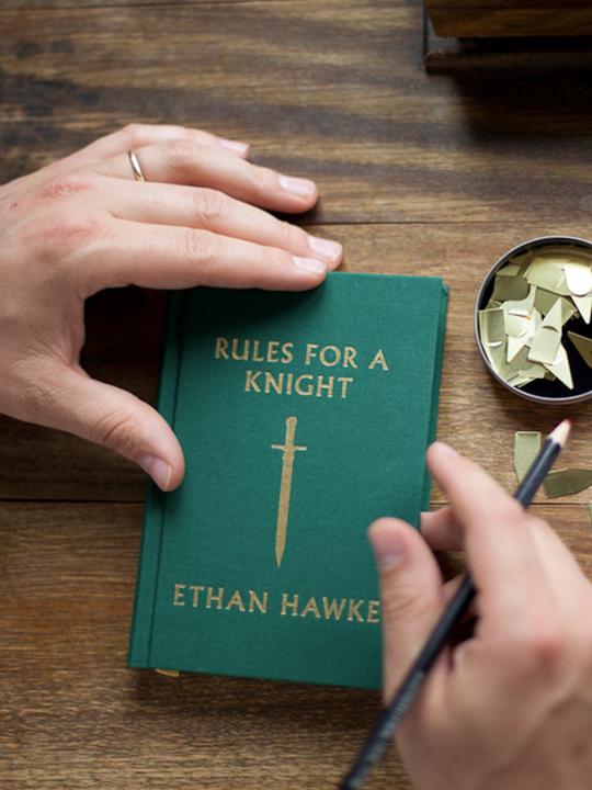 Green hardcover book with gold sword emblem on cover and dangling bookmark ribbon