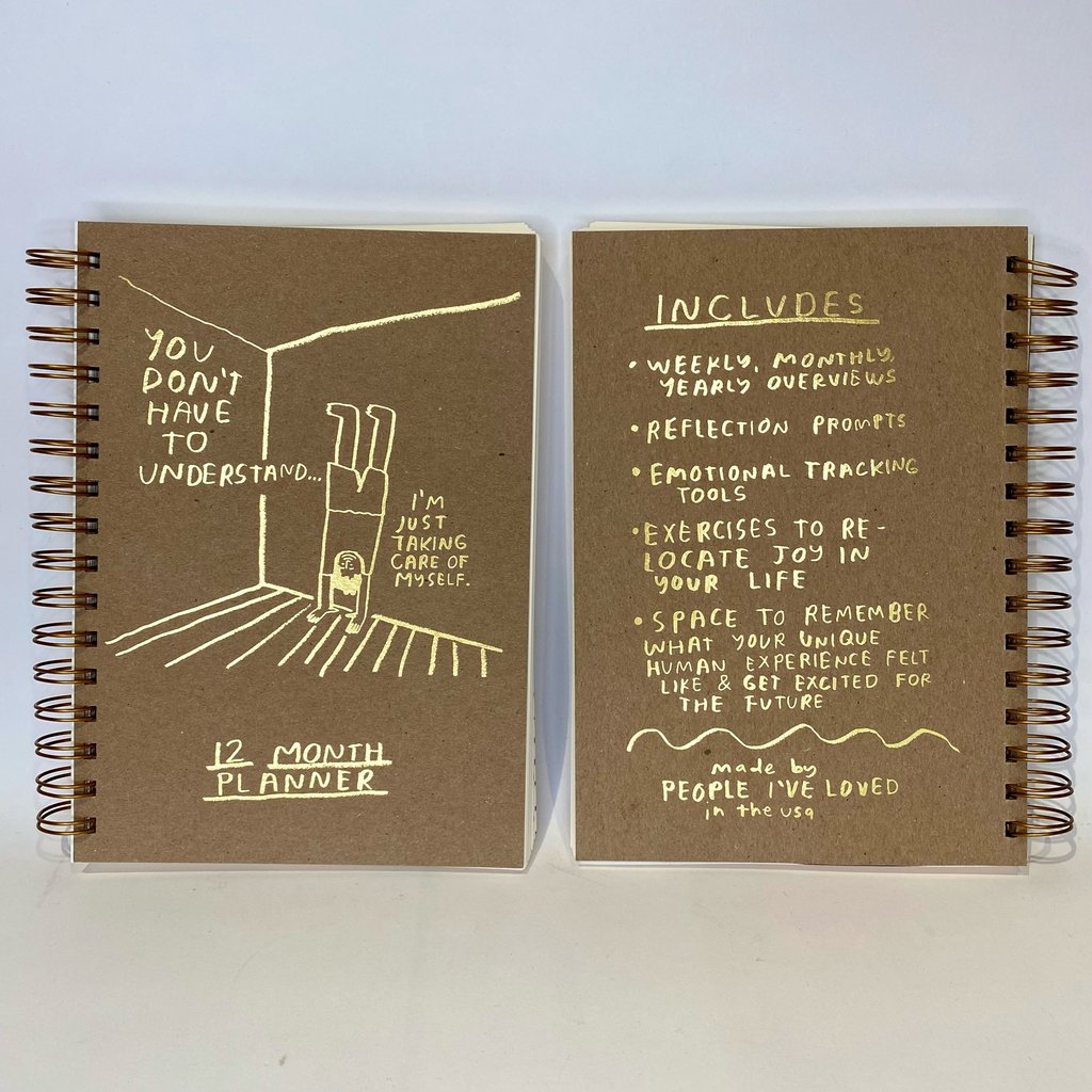 12 month planner notebook open flat; brown covers with yellow text and line-art, spiral binding