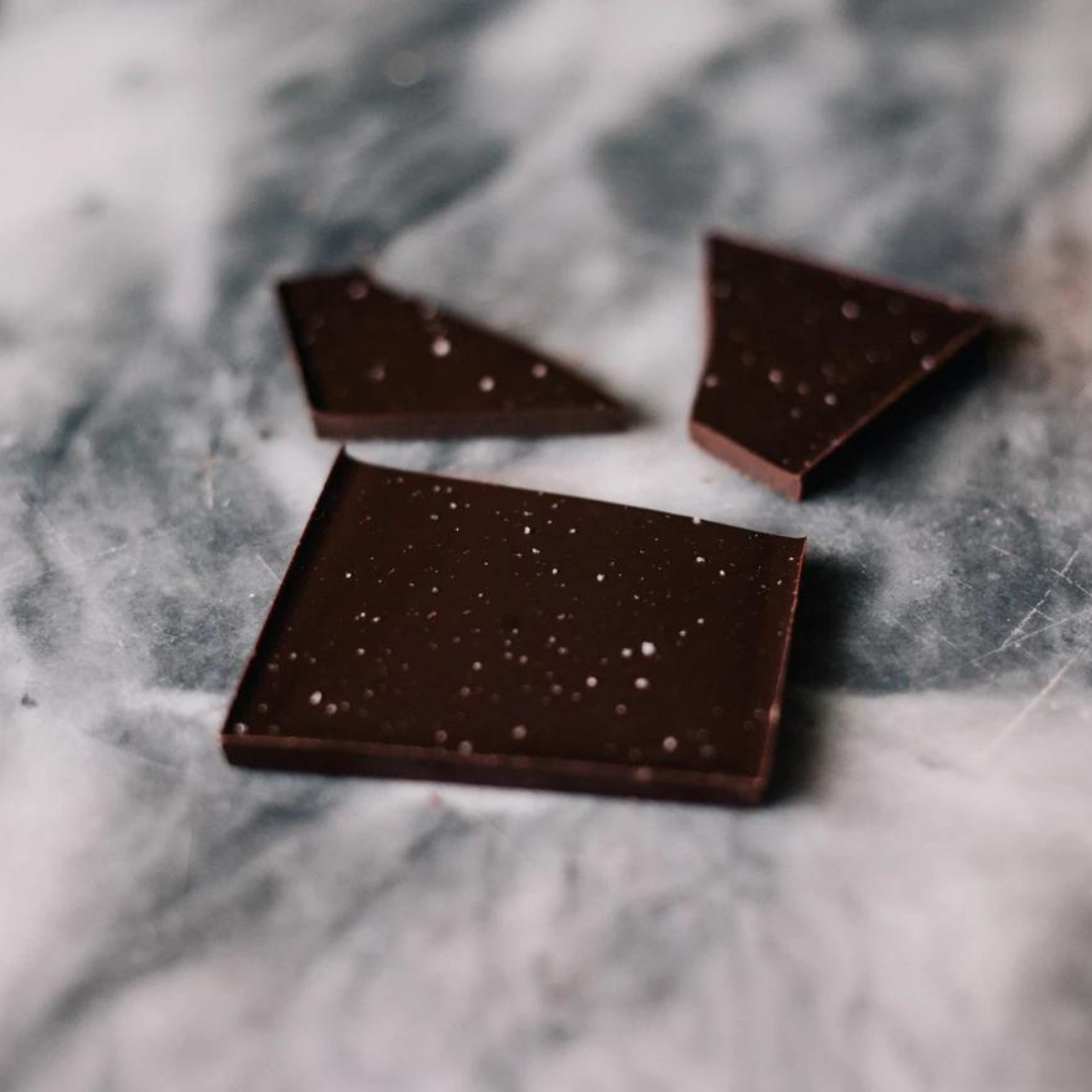 Dark chocolate squares with white salt speckles on gray marble surface