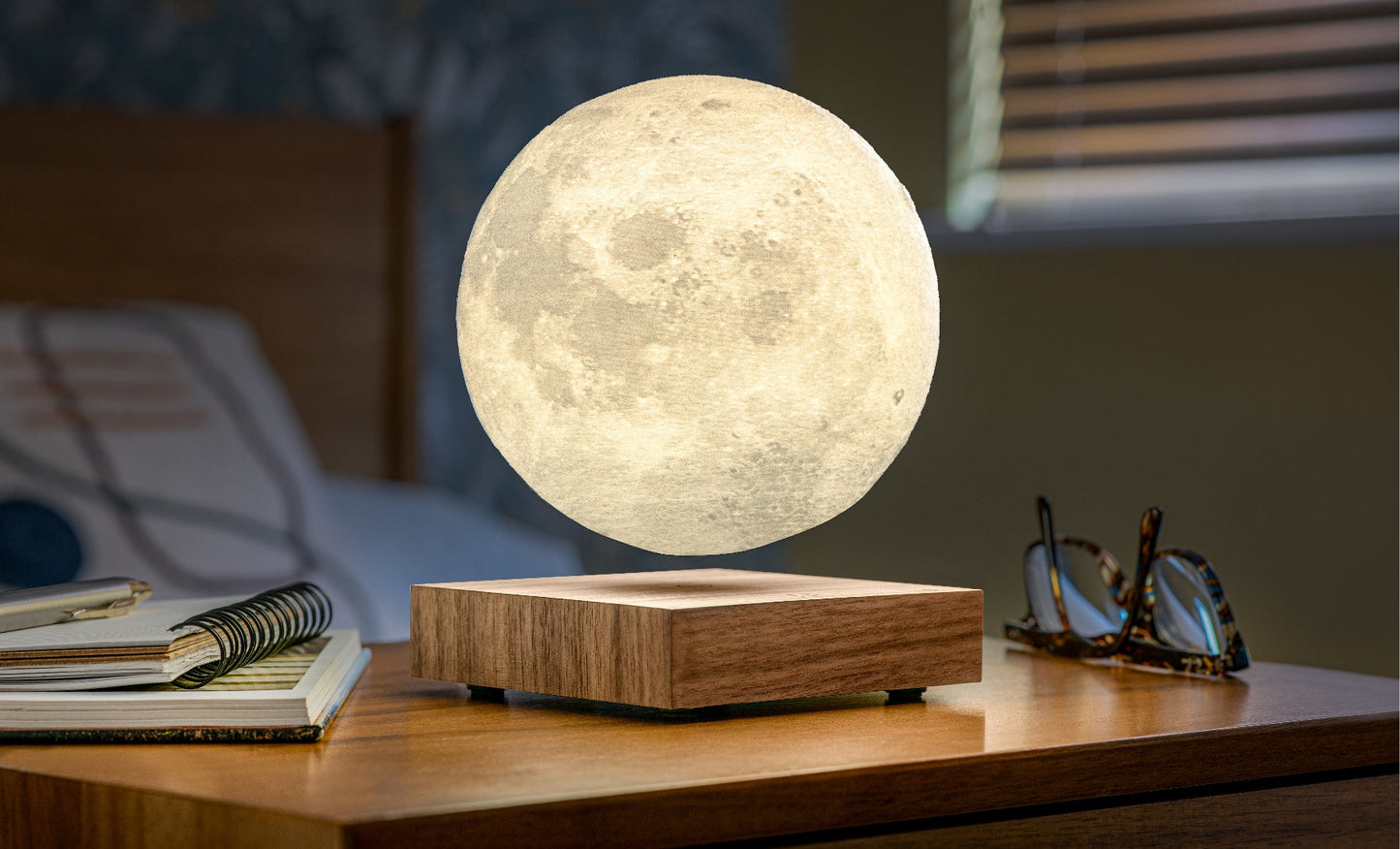 Moon-shaped lamp with glowing white sphere and walnut wood base on desk