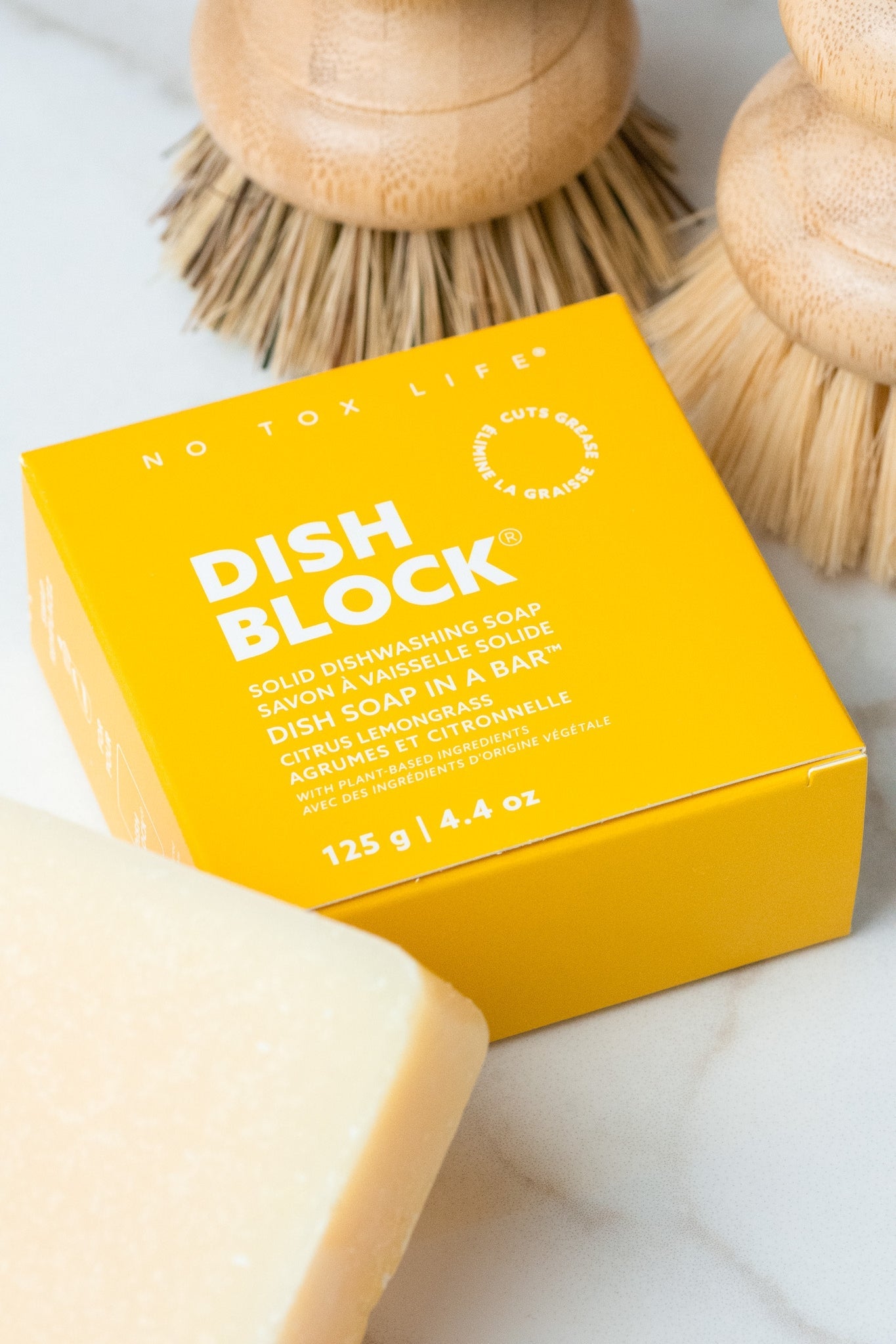 Solid dish soap bar and yellow soap box with wooden scrub brushes.