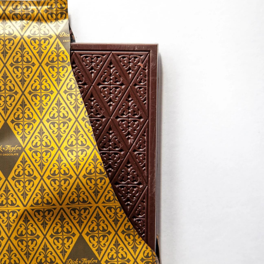 Triangular dark chocolate pieces in box beside yellow patterned wrapper