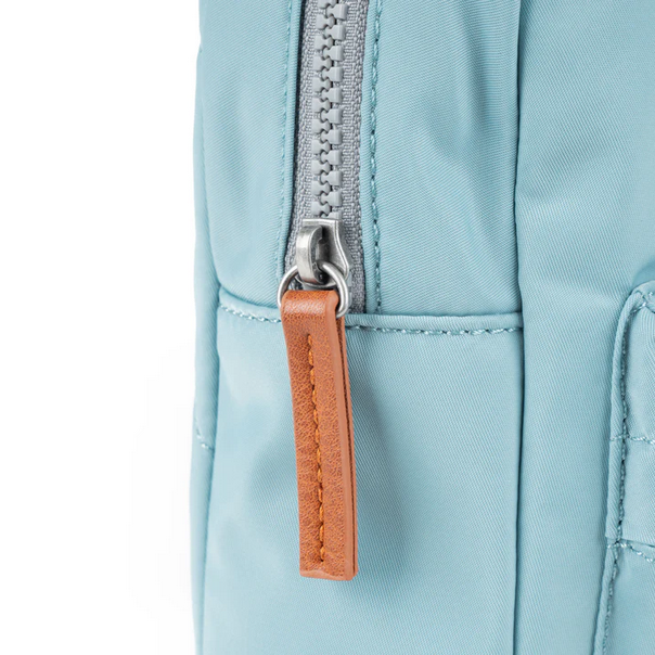 Light blue sling bag close-up with silver zipper pull and brown leather-style tag