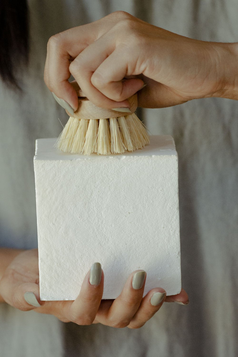 Hand holding a white solid dishwashing soap block with a small scrub brush