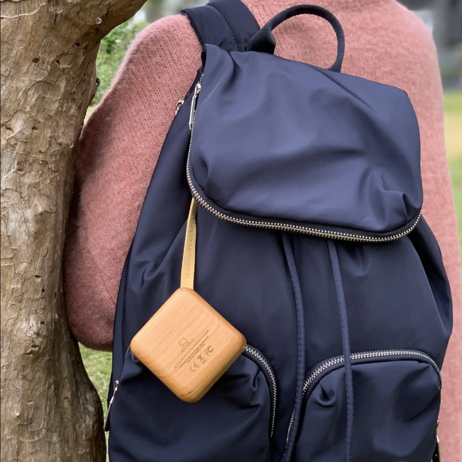 Square bamboo speaker with dark grille, clipped to a navy backpack