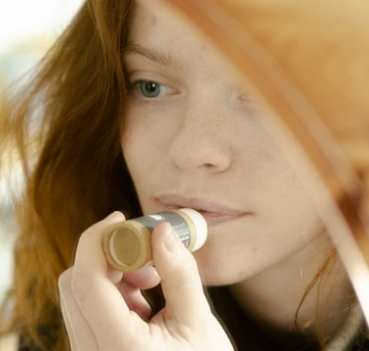Teal lip butter balm with open round cap, creamy beige balm visible