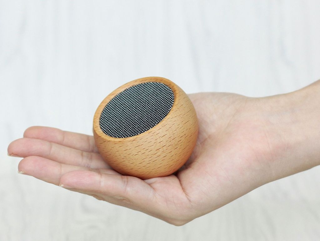 Maple wooden portable speaker with oval fabric grille, held in hand